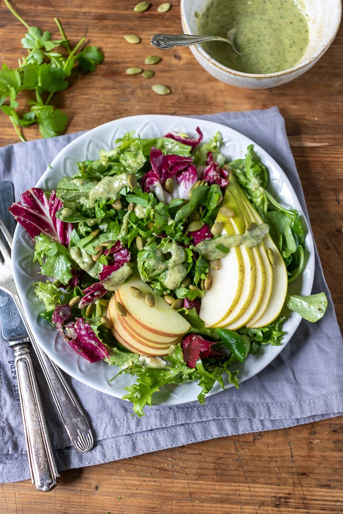 A plate of leafy green salad with radicchio, topped with apples, pears and pumpkin seed dressing