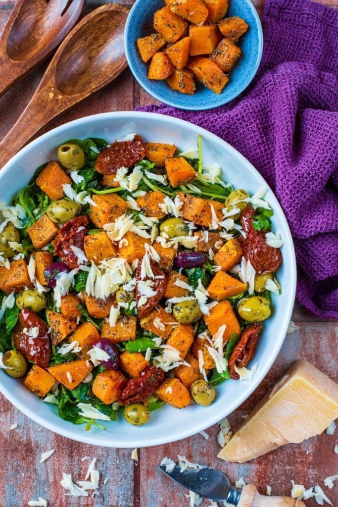 A bowl of roasted butternut squash salad with cheese and sun dried tomatoes. 