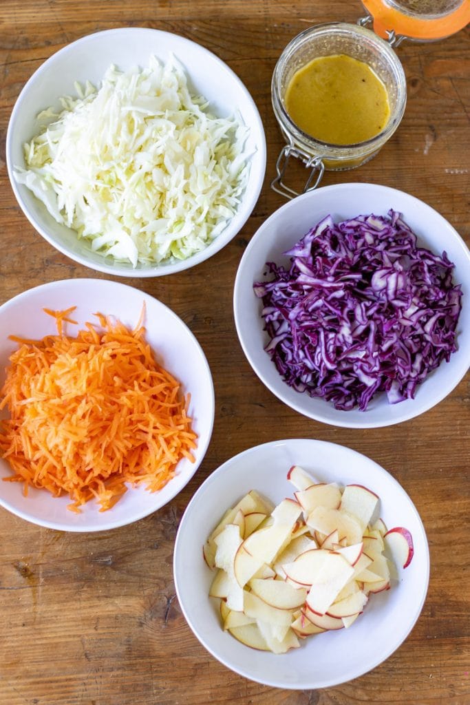 Ingredients for cabbage salad in a bowl - white cabbage, purple red cabbage, carrots, apples, dressing