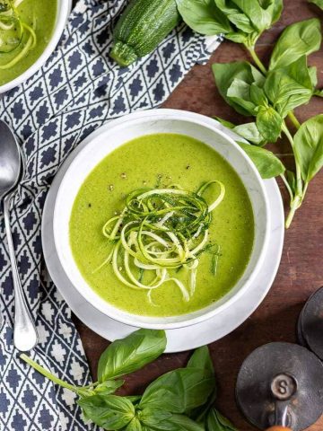 Overhead shot of a bowl of creamy zucchini soup with zoodles on top, surrounded by basil leaves