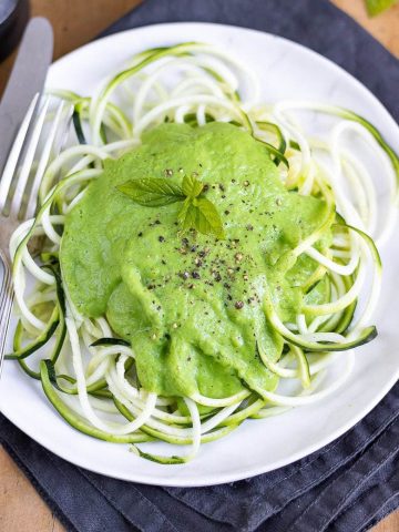 Overhead photo of a white plate of courgetti (spiralised courgette aka zucchini zoodles), with pea sauce on top.