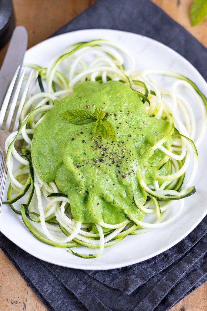 Overhead photo of a white plate of courgetti (spiralised courgette aka zucchini zoodles), with pea sauce on top.