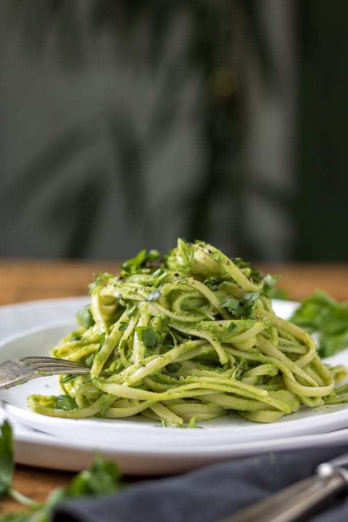 Side view of a plate piled with green pasta - spaghetti tossed in green vegetable herb sauce