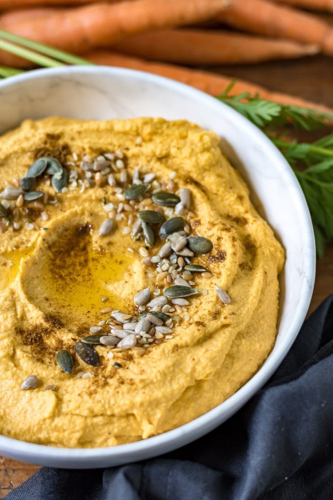 Close up of a bowl of creamy carrot hummus topped with seeds