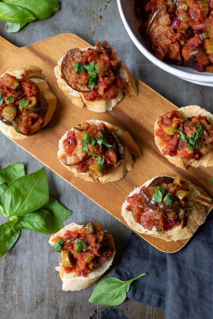 A wooden tray with eggplant caponata siciliana recipe, served on toast as a vegan appetizer