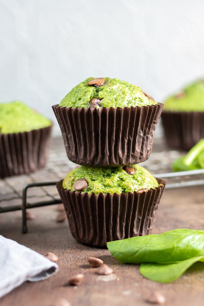 Two Spinach Muffins with chocolate chips stacked on top of each other on a table.
