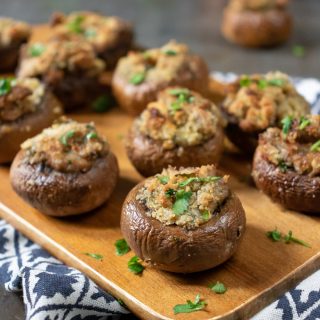 Close up of herb and garlic stuffed mushrooms appetizer recipe on a wooden tray.