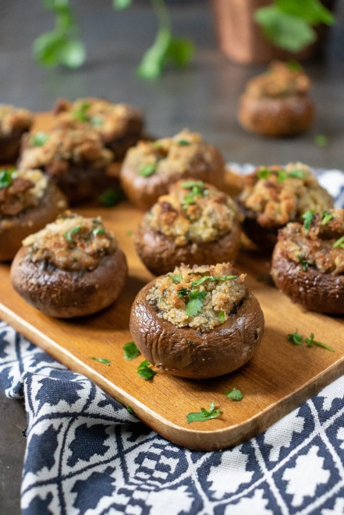 Close up of herb and garlic stuffed mushrooms appetizer recipe on a wooden tray.