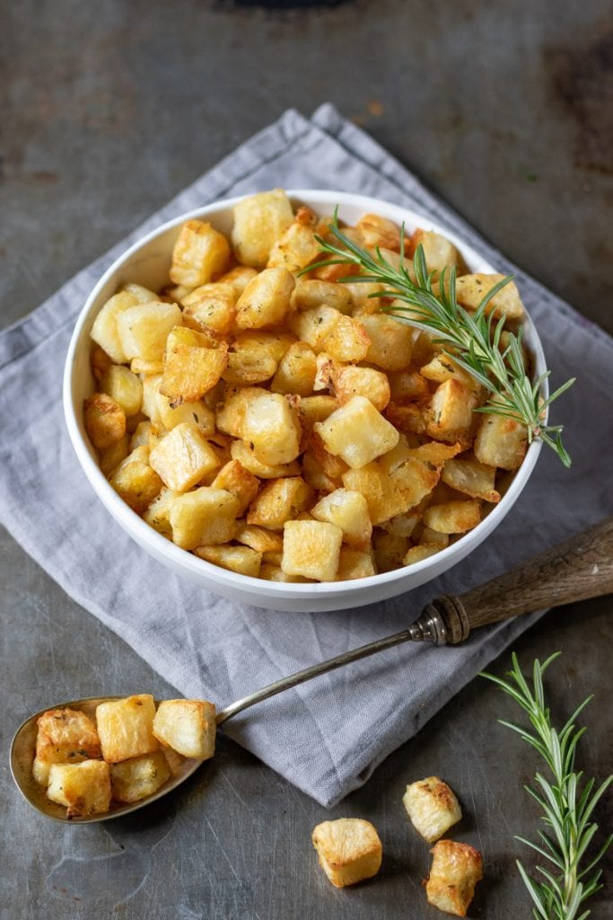 A bowl of parmentier potatoes (roasted diced potatoes recipe) on a grey napkin with sprigs of rosemary.