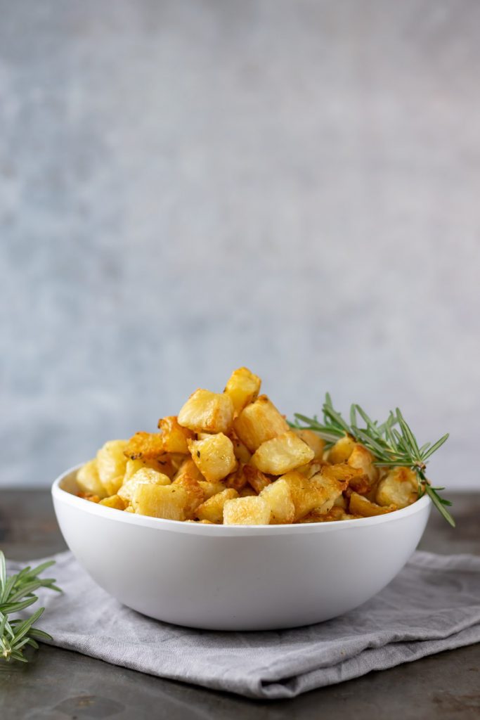 A white bowl filled with parmentier potatoes - small cubes of roasted potatoes with rosemary and garlic.
