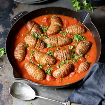 A cast iron skillet with harissa spiced tomato sauce and baked sliced baby Hasselback potatoes