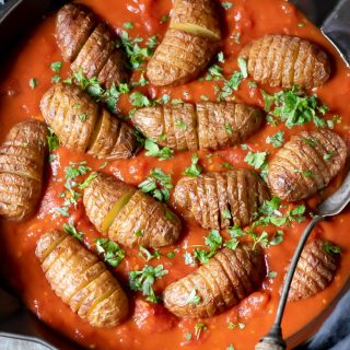 Close up of a cast iron skillet with harissa spiced tomato sauce and baked sliced baby Hasselback potatoes