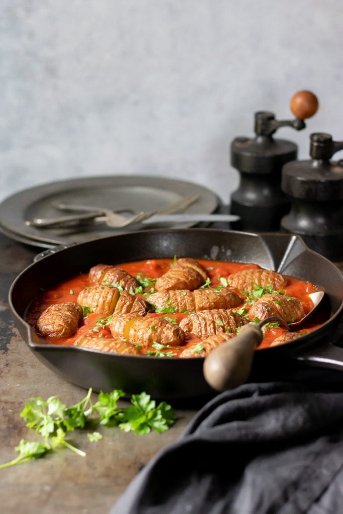 A cast iron skillet with harissa spiced tomato sauce and baked sliced baby Hasselback potatoes recipe