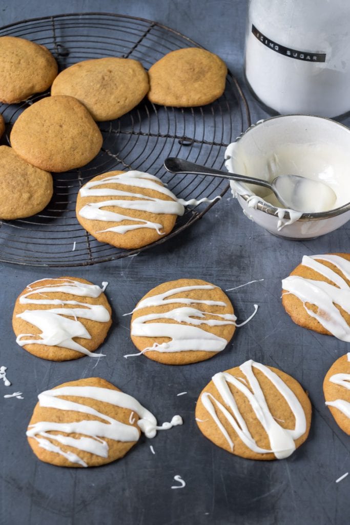 Soft iced pumpkin cookies being drizzled with vanilla icing. 
