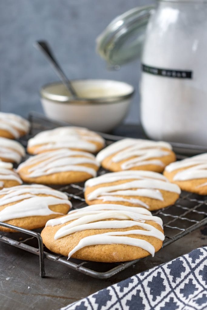 A cooling rack with soft iced pumpkin cookies drizzled with vanilla icing. 