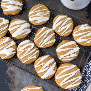 Overhead shot of soft iced pumpkin cookies with vanilla frosting drizzled on them. On a cooling rack.