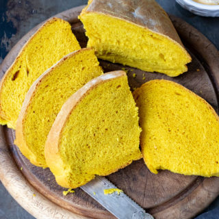 Slices of bright yellow Turmeric Bread on a vintage bread board with an antique knife.