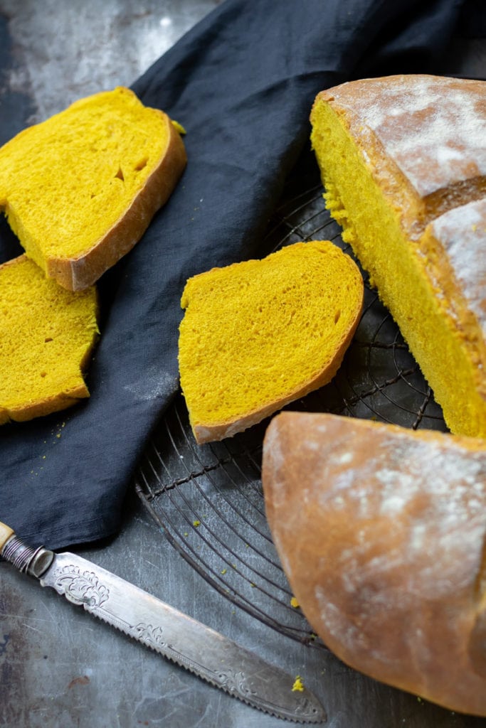 Slices of turmeric bread on a cooling rack next to a linen tea towel.