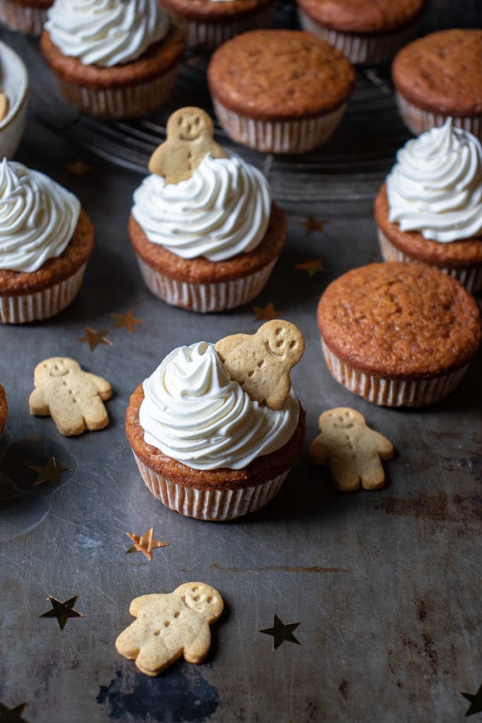 A gingerbread pumpkin cupcake with vanilla frosting and a gingerbread man, with more in the background