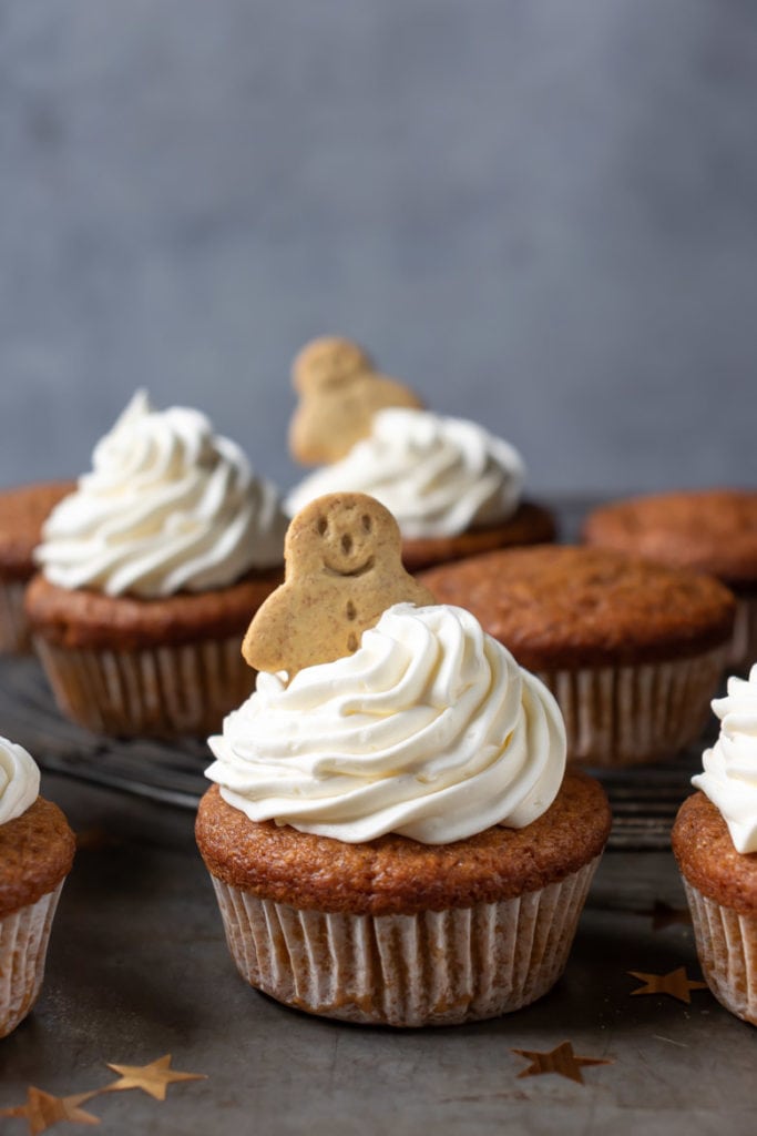 A pumpkin gingerbread cupcake with vanilla frosting and a mini gingerbread man on top. 