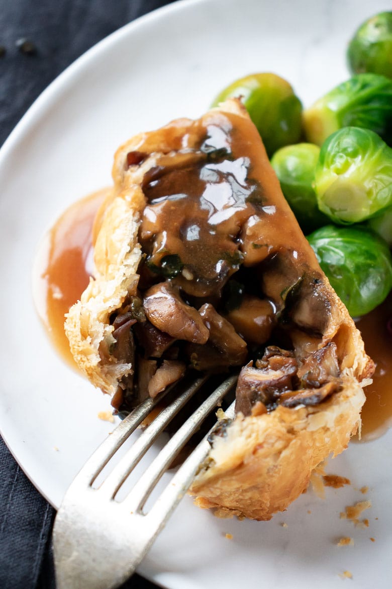 Close up of a slice of vegan wellington with gravy and sprouts.