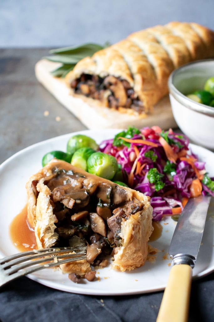 A slice of mushroom wellington on a plate with sprouts and red cabbage.