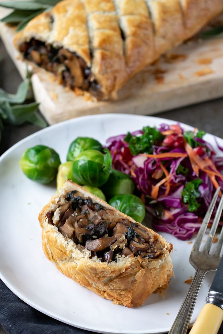 A slice of mushroom wellington on a plate with sprouts and red cabbage salad.