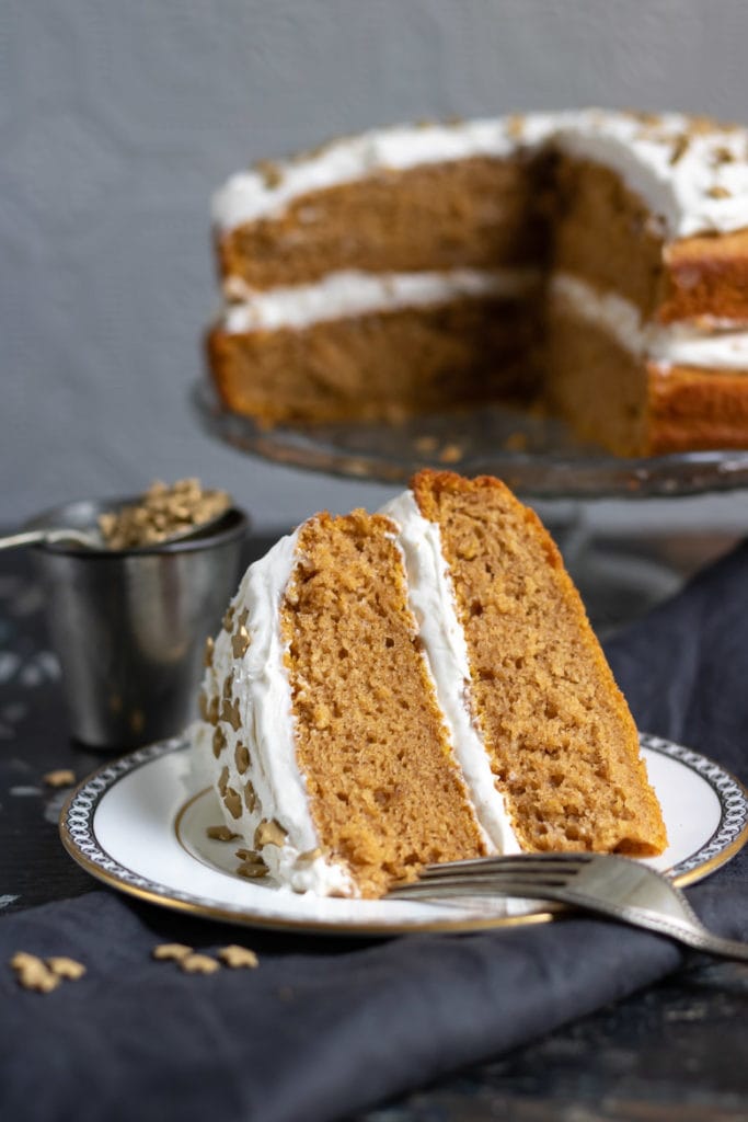 A slice of vegan pumpkin cake with ginger frosting with the layer cake in the background.