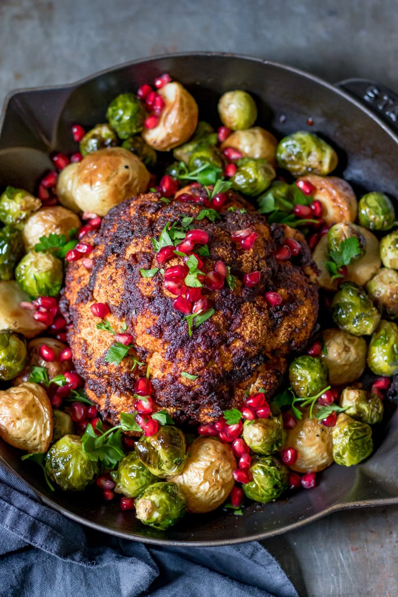 Garlic and Paprika Whole Roasted Cauliflower recipe in a skillet with roasted sprouts, herbs and pomegranate arils.