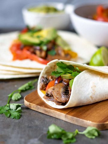 Vegan fajitas with mushrooms and vegetables on a wooden board