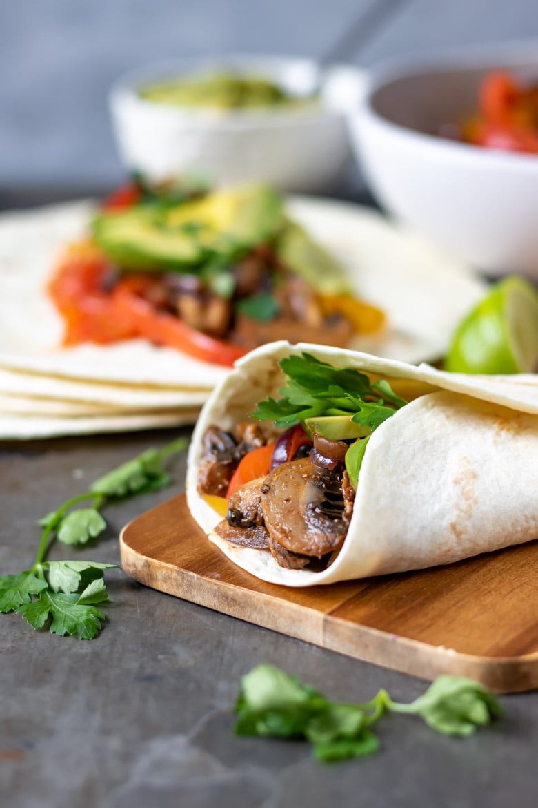 Vegan fajitas with mushrooms and vegetables on a wooden board.