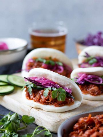 vegan jackfruit bao buns with quick pickled red onions on a board in front of a glass of beer
