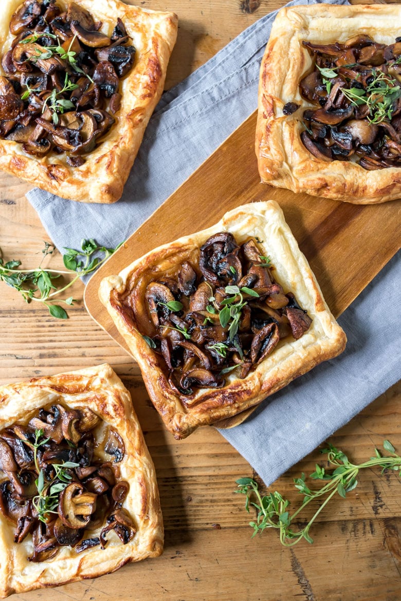 Mushroom tart appetizers made with puff pastry on a wooden table.