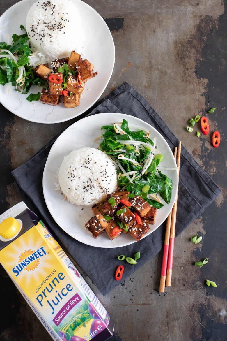 Overhead shot of a table with Asian tofu, greens and rice next to a bottle of Sunsweet Prune Juice.