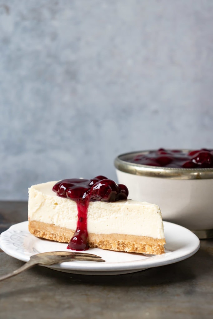 Slice of cheesecake with berry sauce on a plate.