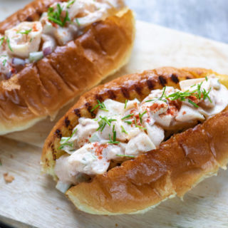 Two vegan lobster roll sandwiches on a wooden board.