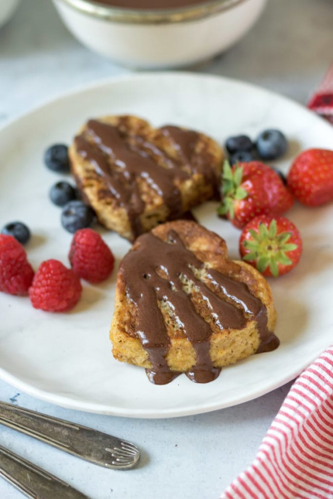 Close up of a plate with heart-shaped french toast, drizzled with chocolate yogurt sauce and berries