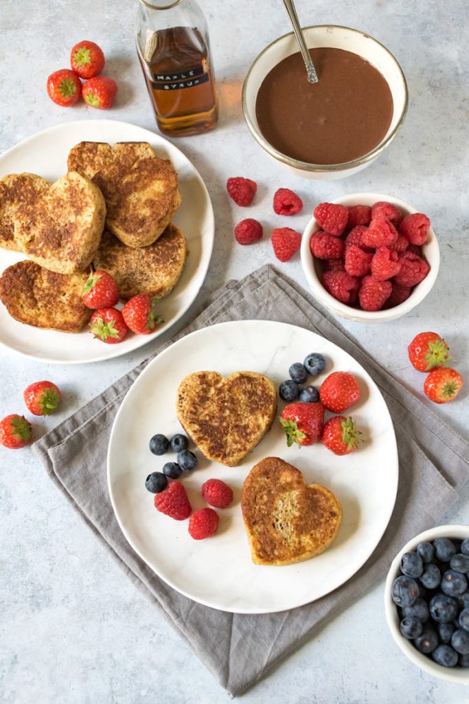 Overhead shot of a plate with heart shaped French toast with berries and chocolate yogurt sauce on the side