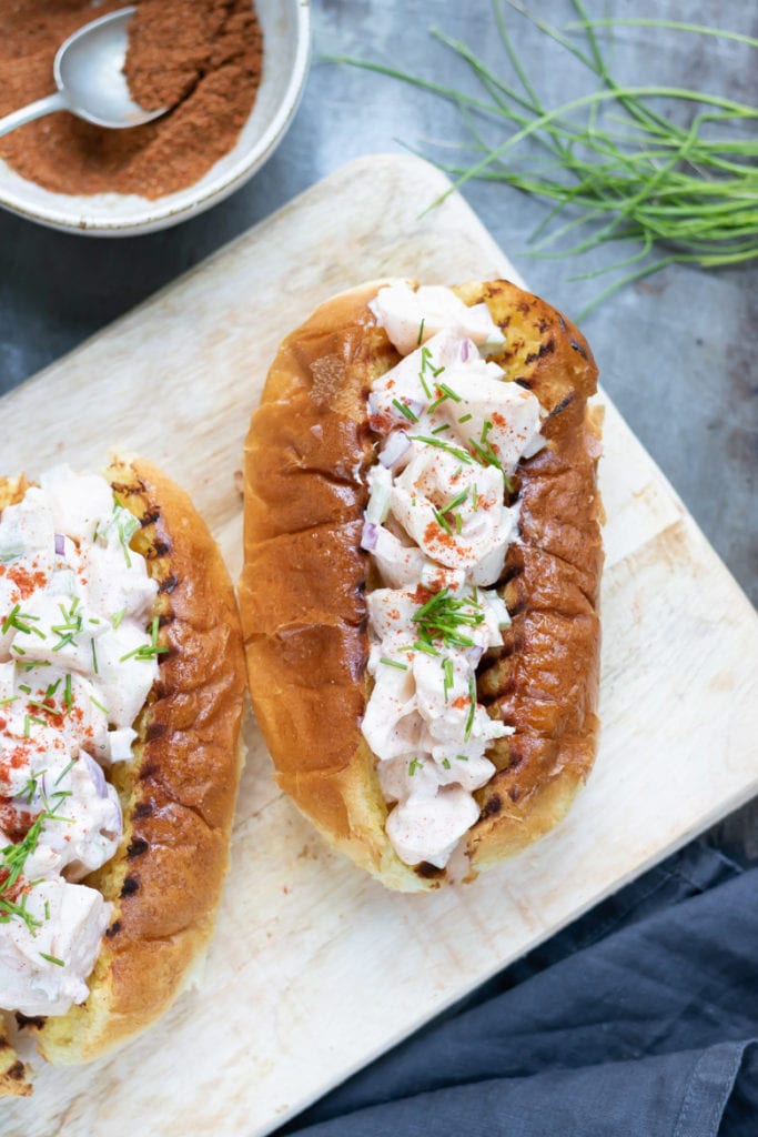 Close up of a vegan lobster roll next to seasoning and chives