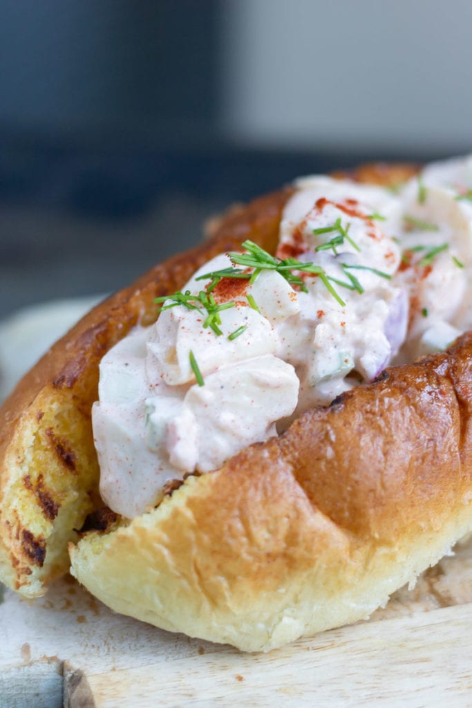 Close up of a vegan lobster roll filled with hearts of palm in a creamy sauce.