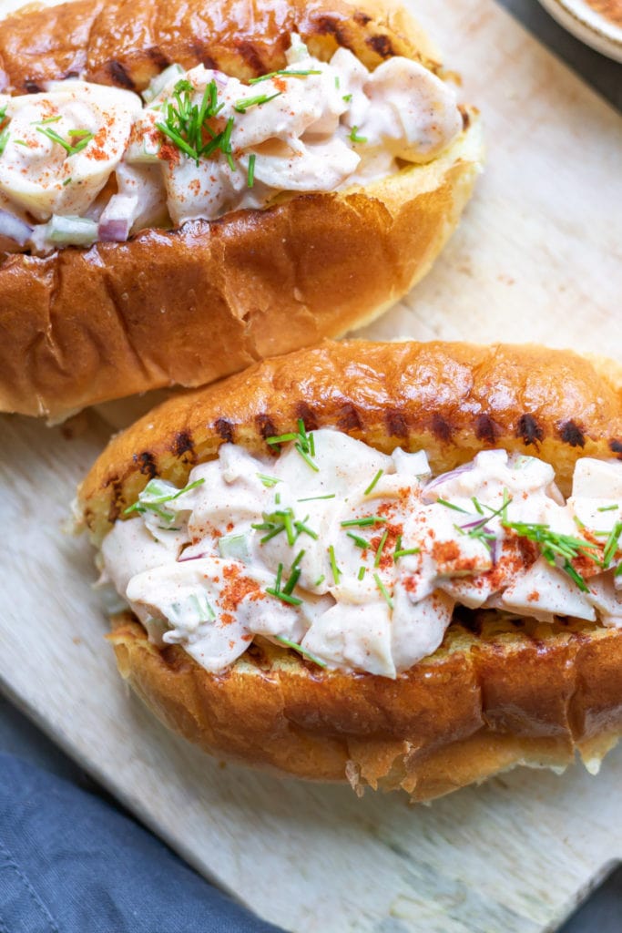 Close up of a vegan lobster roll recipe in a toasted bun, sprinkled with chives and paprika.