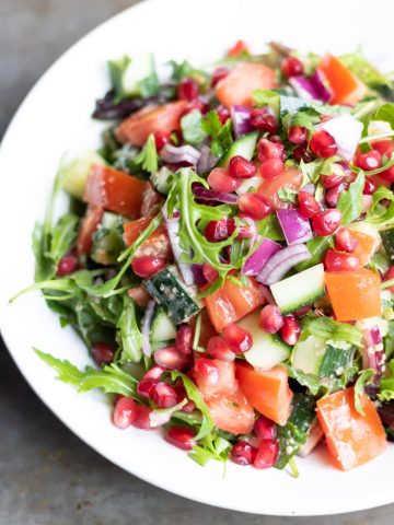 A plate of rocca salad, with rocket arugula, cucumber, tomatoes, red onion, pomegranate and Middle Eastern dressing