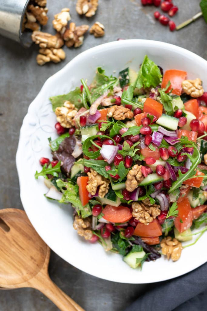 A plate of rocca salad, with rocket arugula, cucumber, tomatoes, red onion, pomegranate and Middle Eastern dressing and walnuts