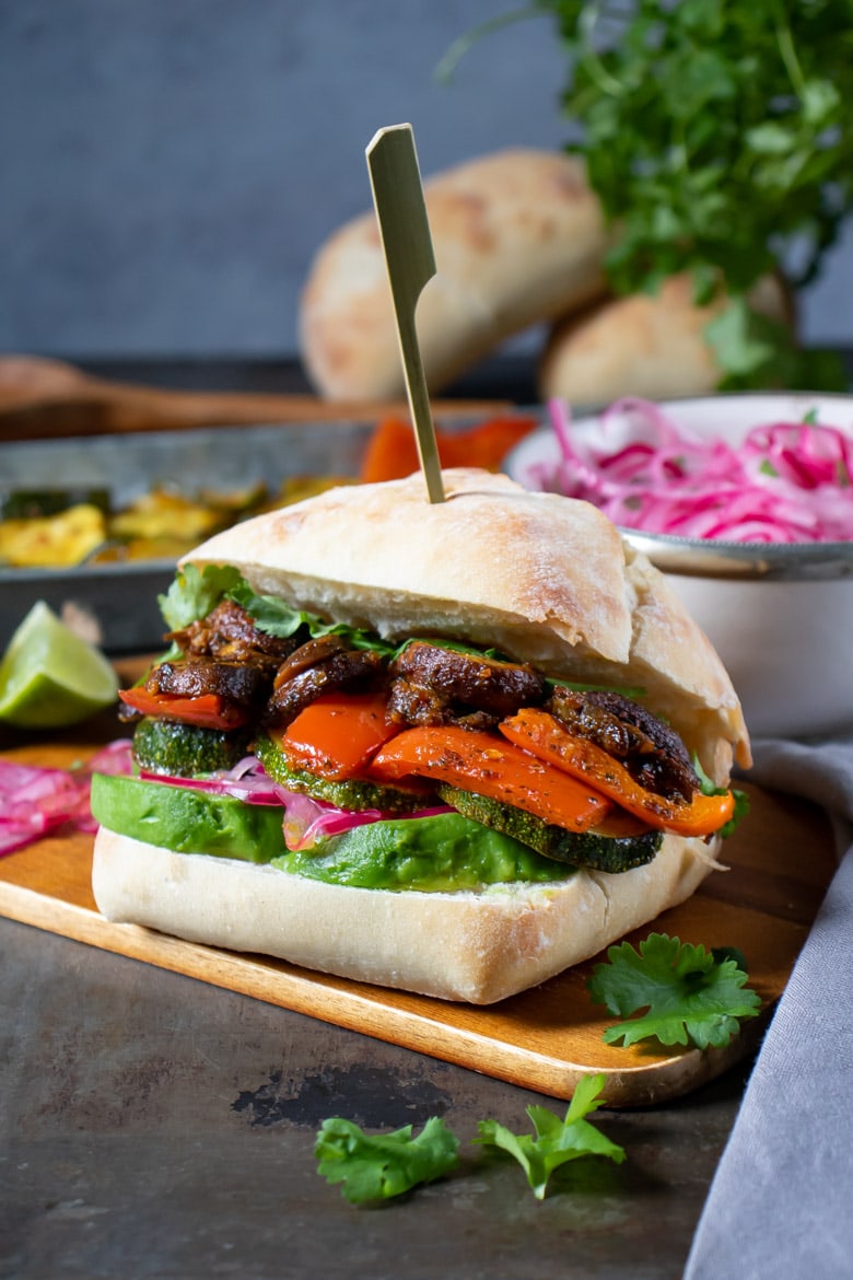 Peruvian sandwich full of spiced vegetables in a roll, with recipe ingredients in the background. 