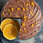 Overhead shot of a chocolate orange cake with orange zest sprinkled on top and a slice missing.