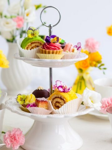 A cake stand full of food for afternoon tea, with tea cups and flowers.