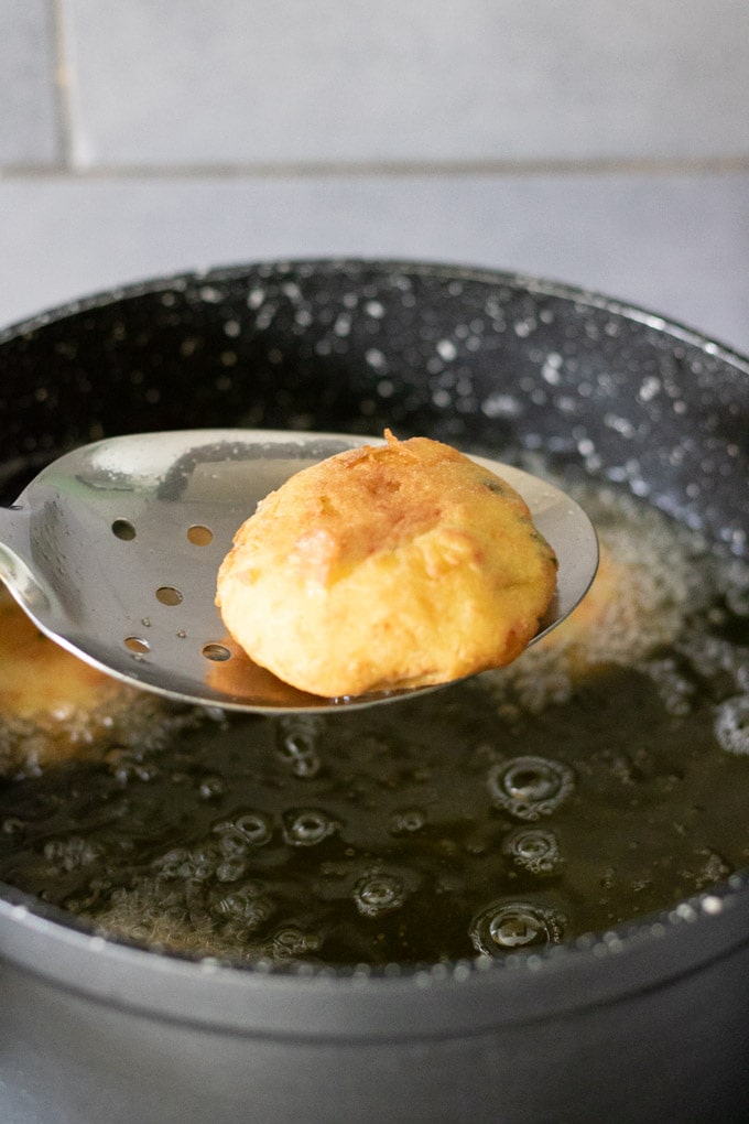 A maakouda potato cake on a spoon being lifted out of hot oil