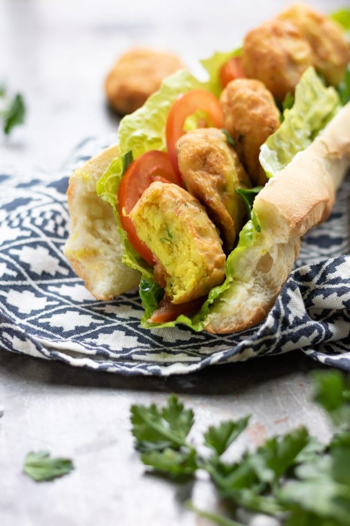 Fried potato cakes in a baguette with lettuce and tomato, with a bite out.