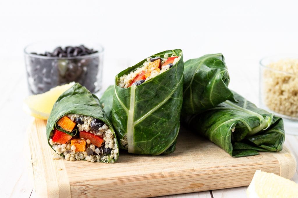 collard wraps with quinoa and sweet potato cut on a wooden board.