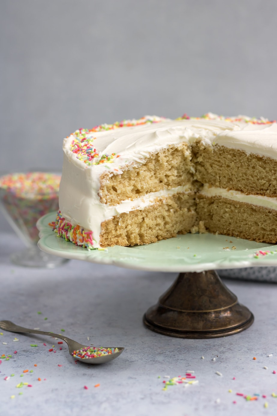 Vegan layer cake with slices removed, on a cake stand